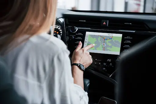 A person in the driver’s seat uses a touchscreen car navigation system, pointing at a map displayed on the screen inside a modern vehicle.