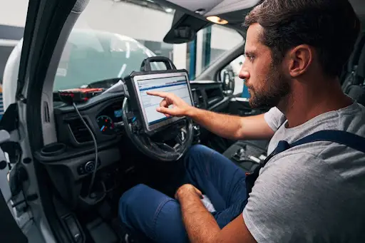 A man sits in the driver’s seat of a car, using transportation management software on a diagnostic tablet mounted to the steering wheel to check vehicle data. He is focused and appears to be working or troubleshooting.